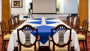 Un salón de conferencias con una mesa larga, sillas, una pantalla de proyector y una pizarra.