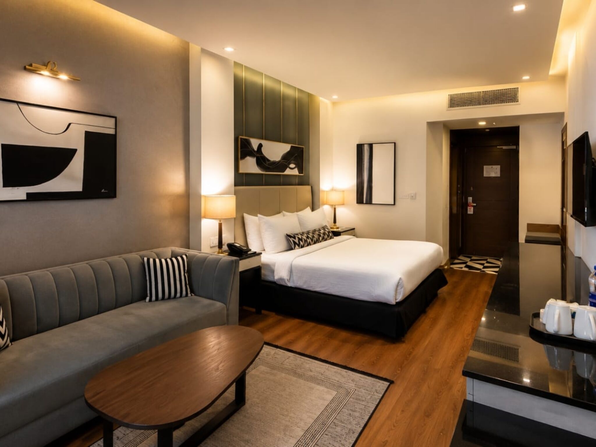 A modern hotel room with a bed, a sofa, a coffee table, and a TV.