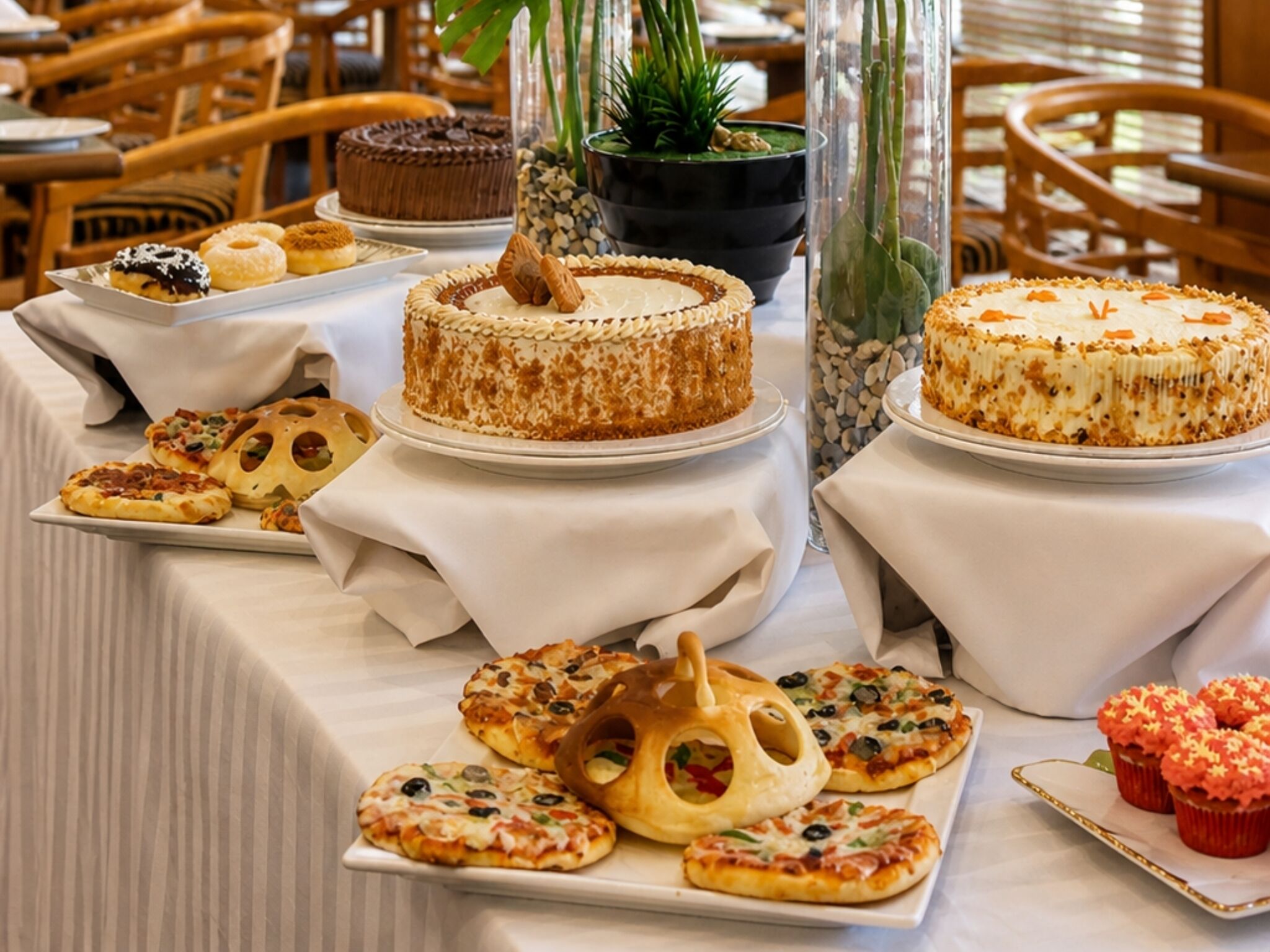 A buffet table with various desserts and pizzas.