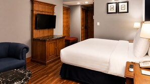 Una habitación de hotel con una cama, un televisor montado en un mueble de madera, un escritorio con una lámpara y una silla.