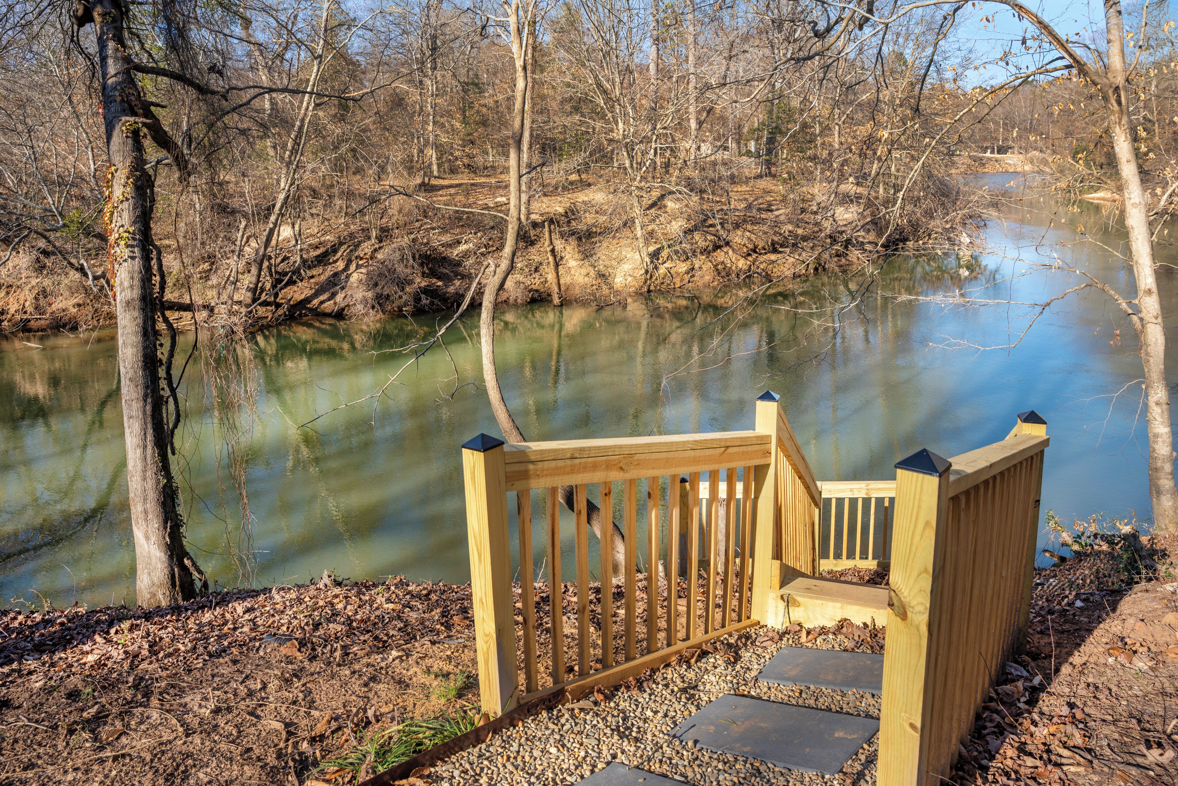 A wooden bench overlooking a calm river with trees in the background.