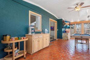 Ein Zimmer mit Billardtisch, Deckenventilator und großem Fenster.