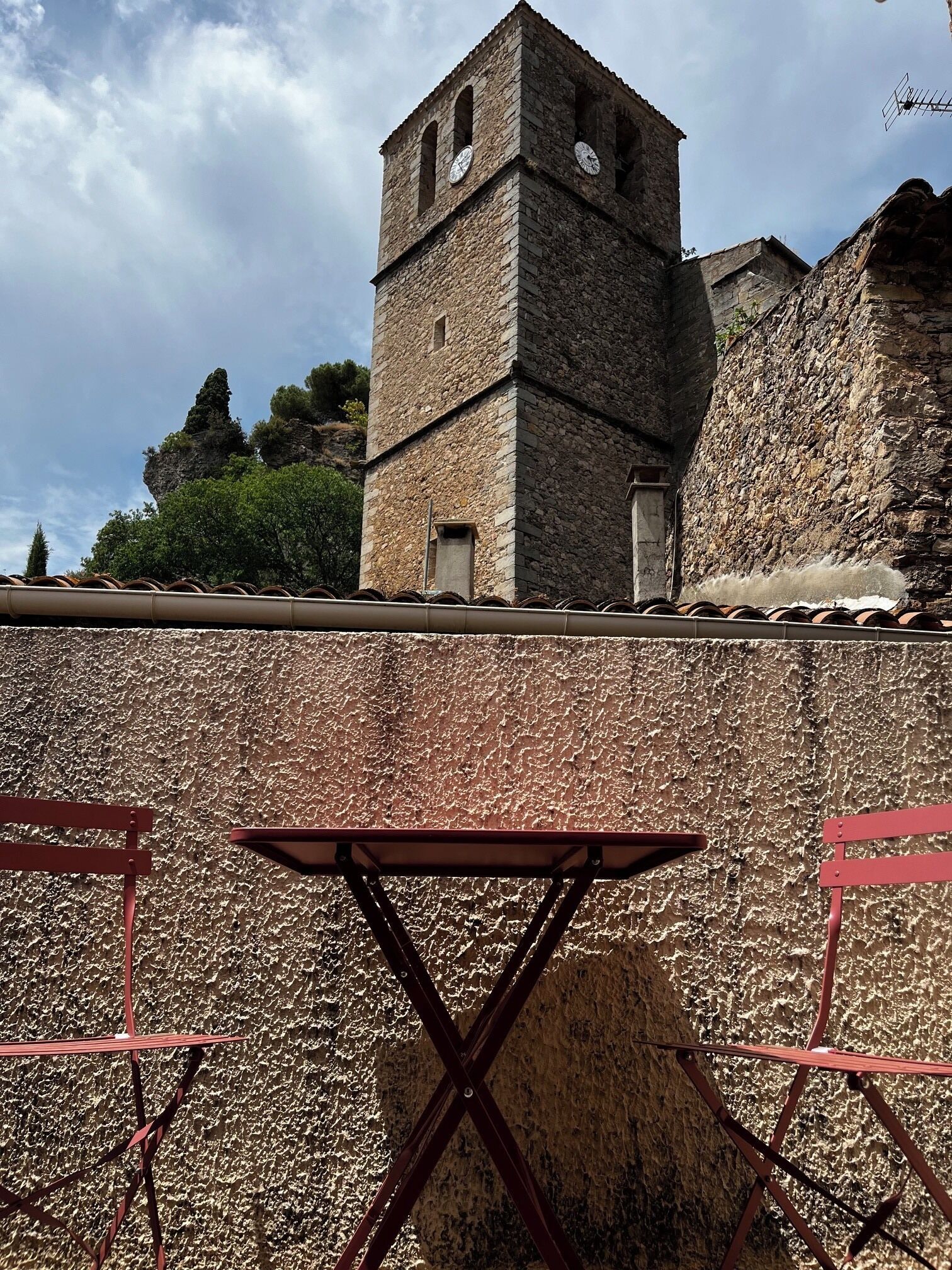 A stone tower with a clock, a red metal table, and red metal chairs.