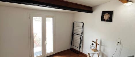 Une pièce avec un plancher en bois, un canapé vert, un plafond avec des poutres apparentes et une porte donnant sur l’extérieur.