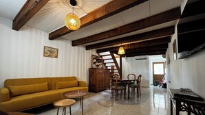 A living room with a sofa, a coffee table, and a dining area with chairs and a table. - A house in the heart of the village of Mourèze, just a stone's throw from the Cirque. (Mourèze)
