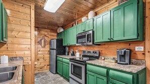 Uma cozinha compacta com armários verdes, eletrodomésticos de aço inoxidável e bancada de granito.