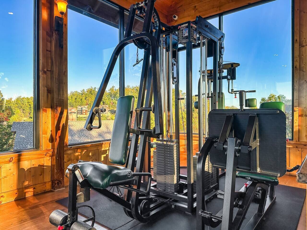 A gym with various exercise equipment, large windows, and a view of trees.