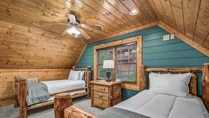 A cozy cabin room with two wooden beds, a ceiling fan, and a window with blinds. - Mt LeConte Views + Hot Tub + Game Room (Sevierville)