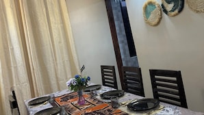 A dining area with a table set for four, including plates, glasses, and cutlery. There are three wall-mounted decorative items and a ceiling light fixture.