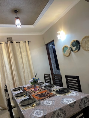 A dining area with a table set for four, including plates, glasses, and cutlery. There are three wall-mounted decorative items and a ceiling light fixture.