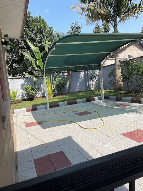 A courtyard with a tiled floor, a green canopy, and surrounding greenery.
