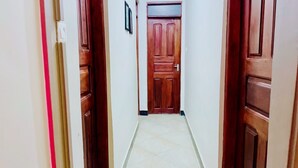 A hallway with a wooden door at the end, white walls, and a tiled floor.
