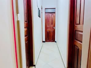A hallway with a wooden door at the end, white walls, and a tiled floor.