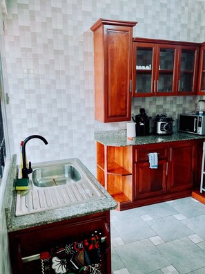 A kitchen with a granite countertop, a sink, wooden cabinets, and a microwave.