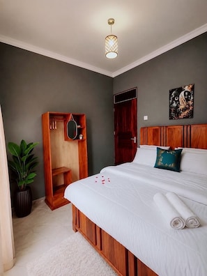 A hotel room with a bed, a wooden wardrobe, a mirror, a potted plant, and a painting on the wall. - Jubilant Experience Homes | Elegant 3BR Retreat in Arusha🇹🇿🗻🦒 (Arusha)