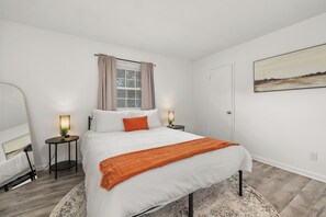 Une chambre à coucher comprenant un lit, des tables de chevet, une fenêtre avec des rideaux, une porte et un tableau accroché au mur.