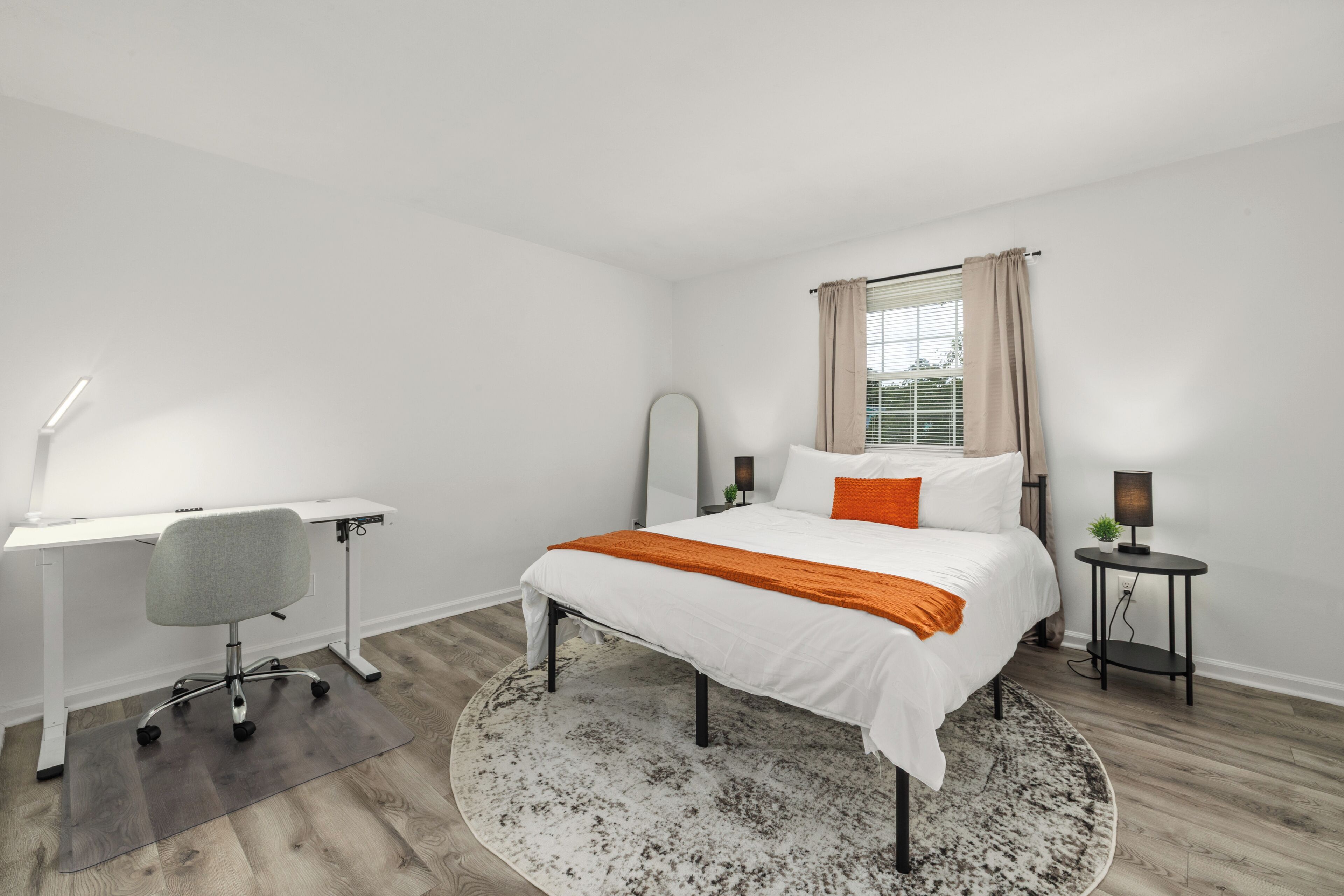 Un dormitorio con cama, escritorio, silla y una mesita con lámpara.