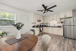 Une cuisine moderne avec des armoires blanches, un réfrigérateur en acier inoxydable et un ventilateur de plafond.