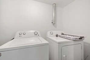 A laundry area with a front-loading washer and dryer, control knobs, and a vent pipe above the dryer. - Durham Home Near Duke-Fast WiFi & Self Check-In (Durham)
