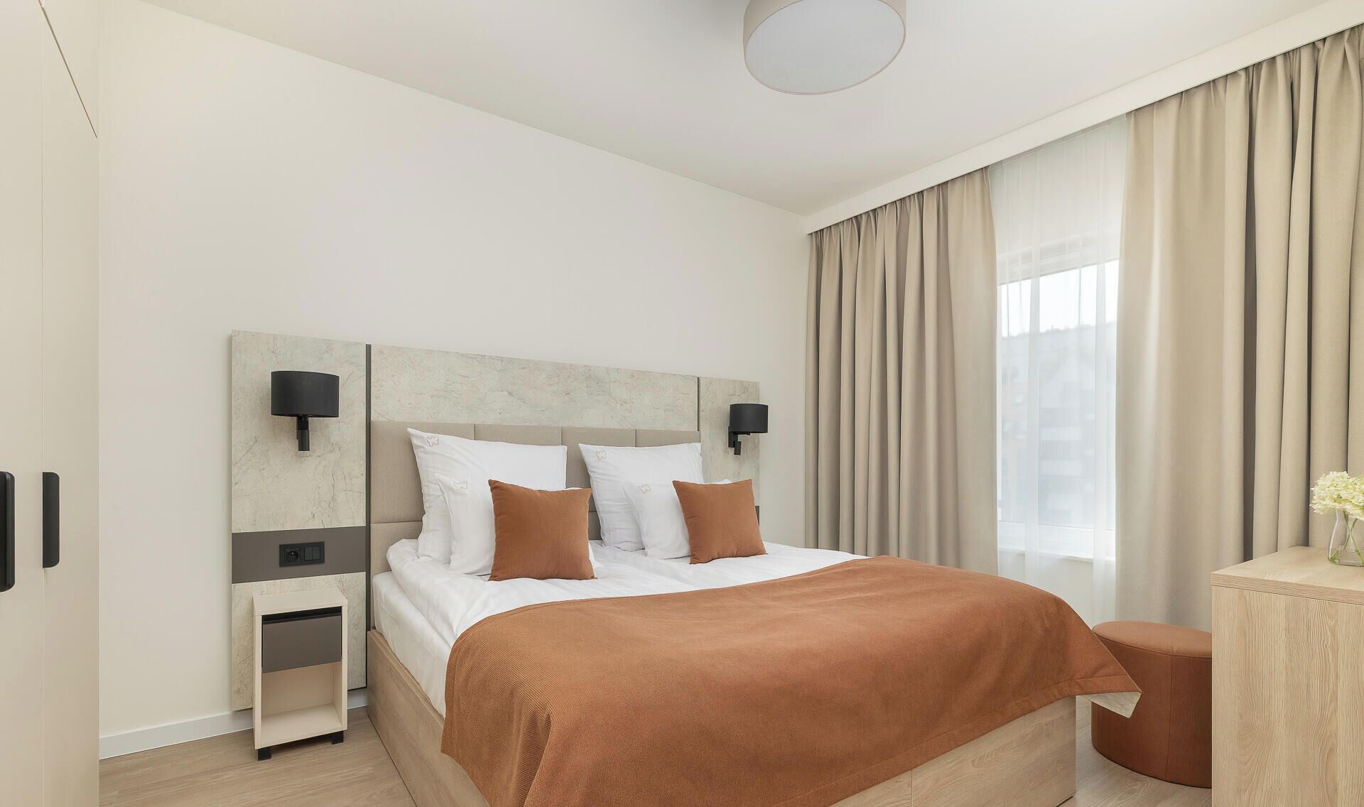 Een moderne hotelkamer met een groot bed, nachtkastjes, een klein tafeltje en uitzicht op de stad.
