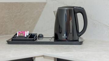 A black coffee maker on a countertop with a tray holding a pink packet and a black object, possibly a remote control.