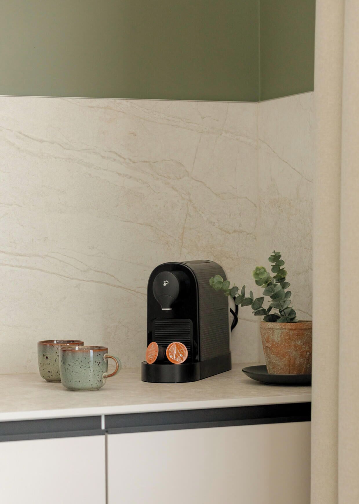 A kitchen with a coffee maker, two mugs, and a potted plant.