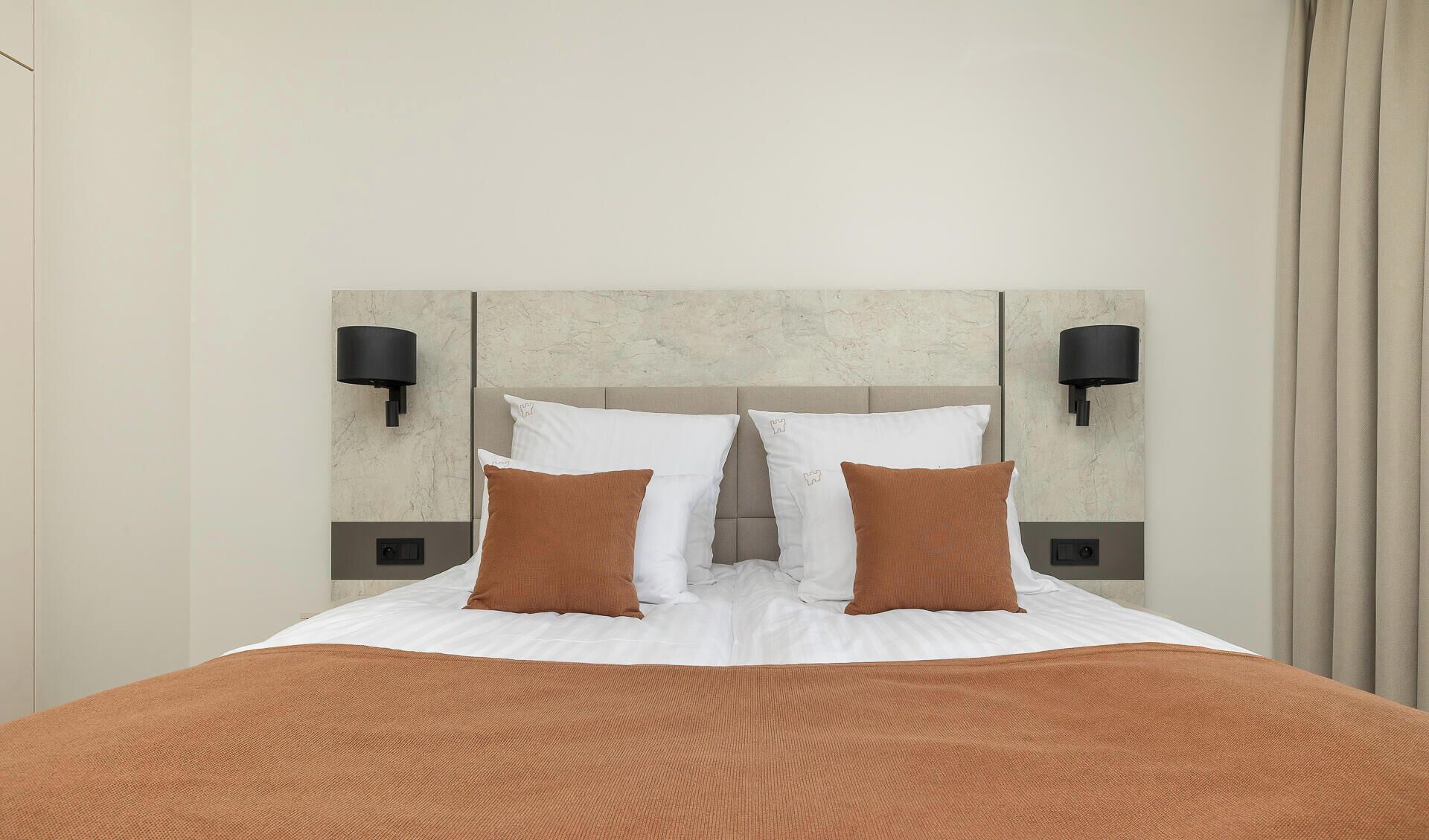 A hotel room with a large bed, two wall-mounted lamps, and a headboard with a textured design.