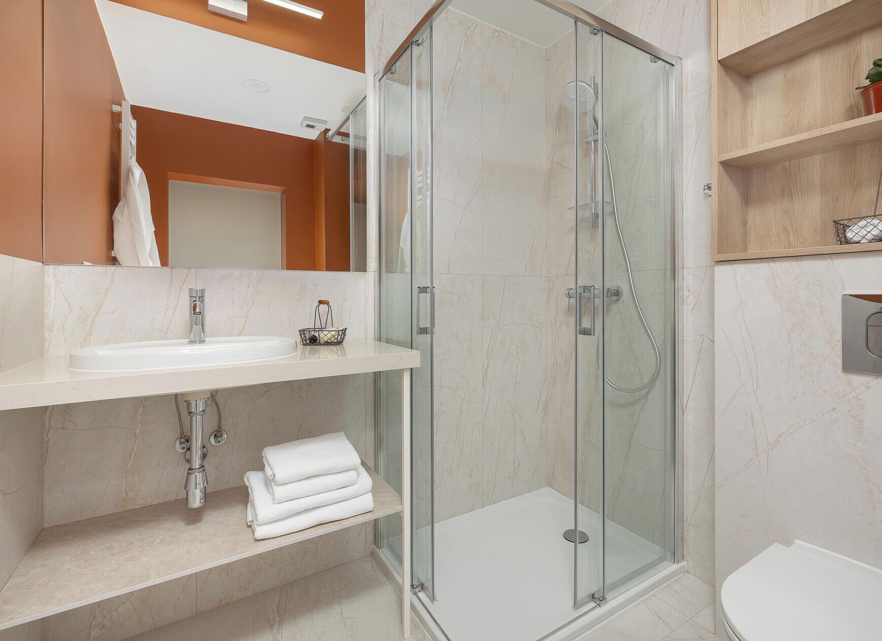Un baño moderno con ducha envuelta en vidrio, lavamanos blanco y retrete.