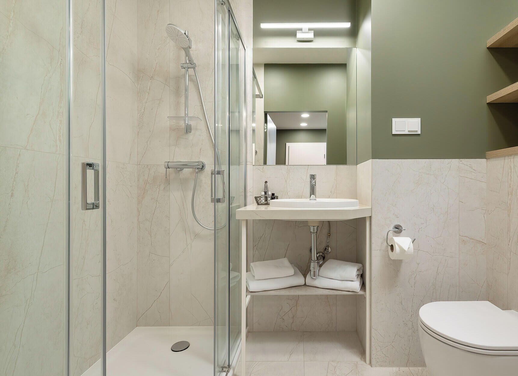 Un baño moderno con ducha envuelta en vidrio, un lavamanos blanco y un inodoro.