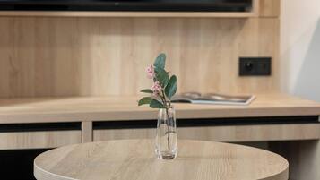 Een ronde tafel met een glazen vaas met plant en groene bladeren en roze bloemen.