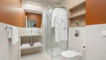 Un baño moderno con cabina de ducha de vidrio, inodoro blanco y tocador con espejo y lavabo.