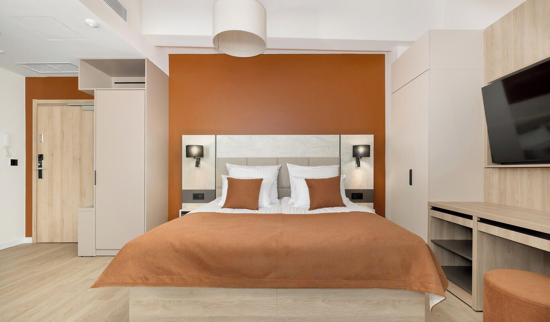 A modern hotel room with a large bed, a TV, and a desk.