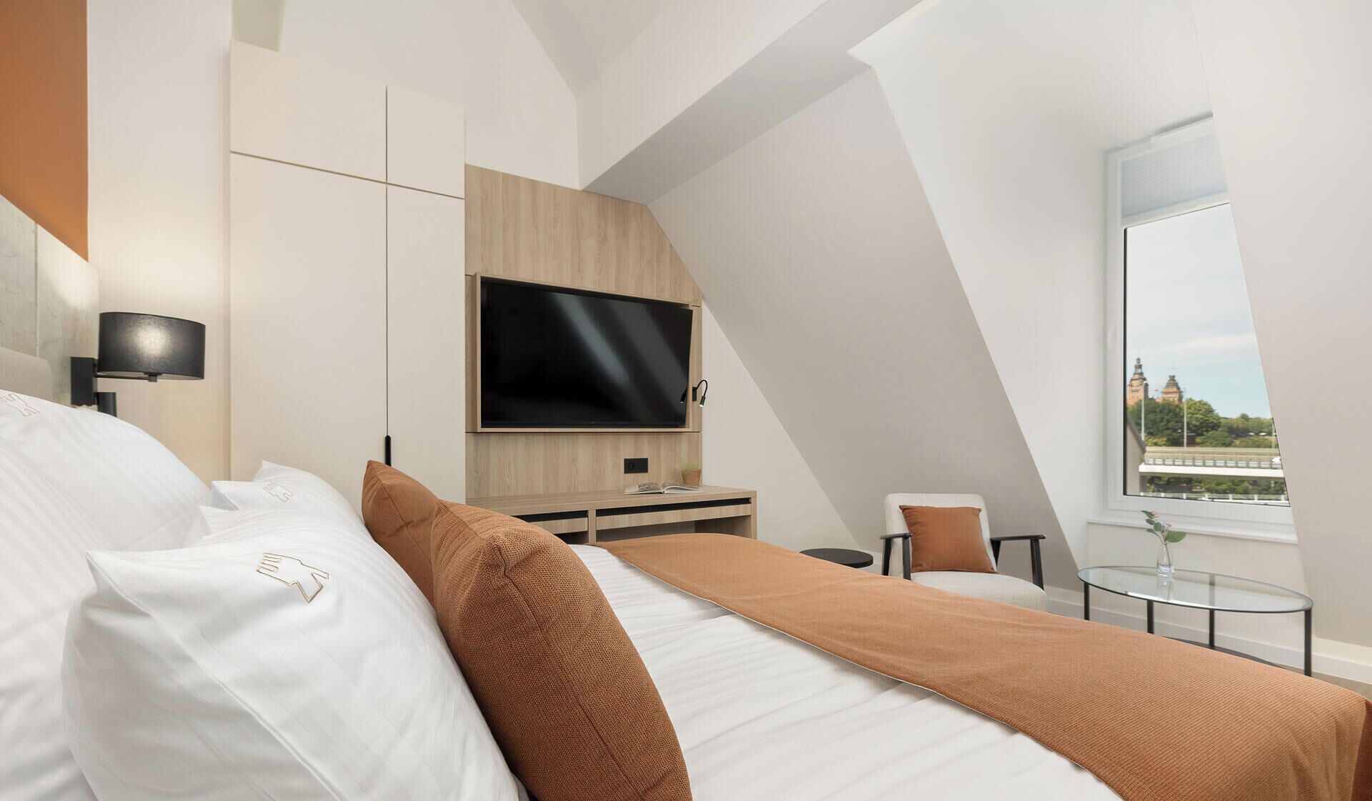 Habitación de hotel moderna con cama, televisor de pantalla plana, una mesita y ventana con vistas.