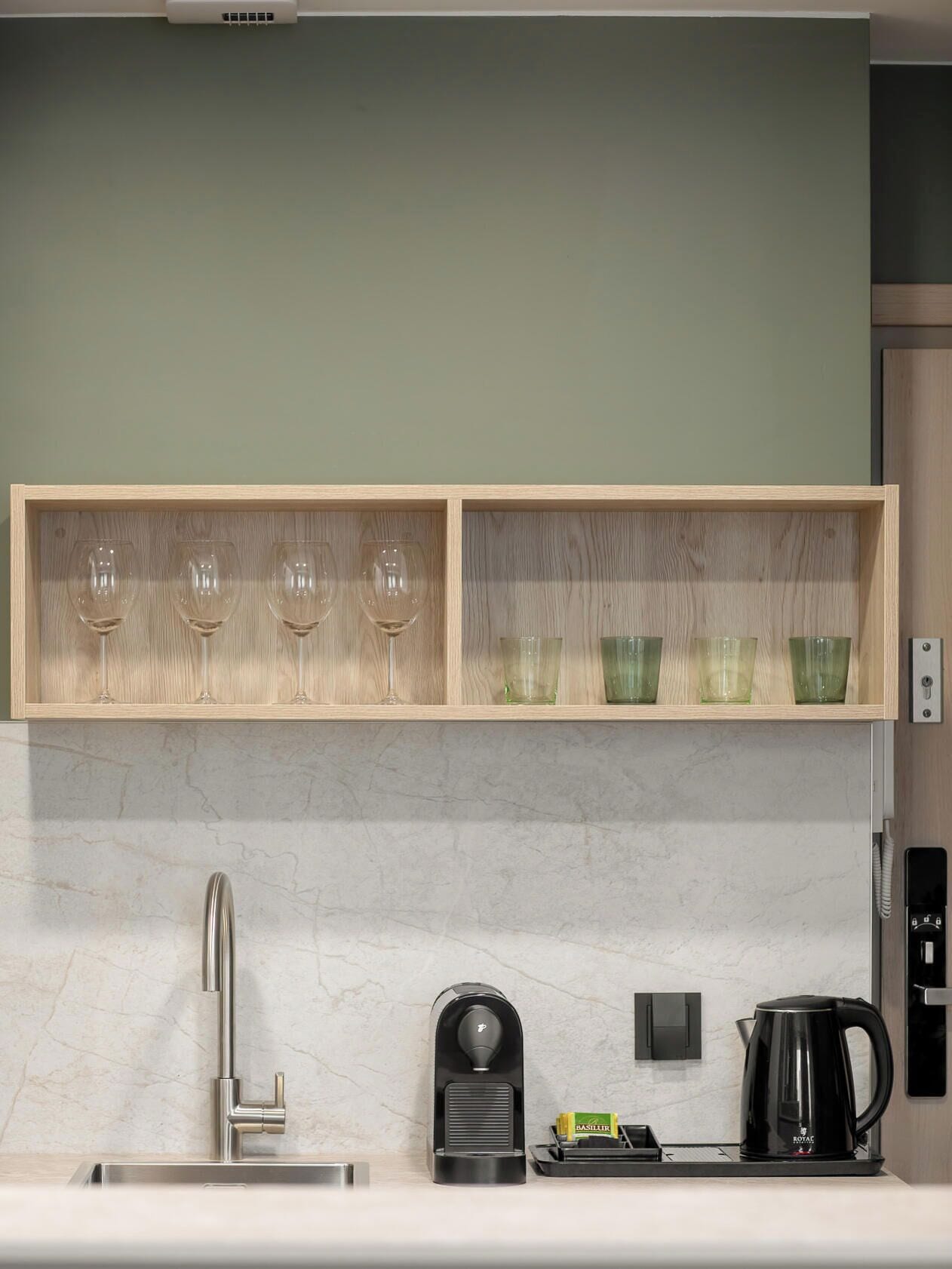 Een keuken met een marmeren aanrecht, een moderne kraan, een koffieapparaat en een plank met wijnglazen en groene bekers.
