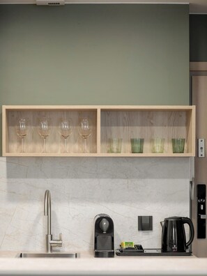 Una cocina con encimera de mármol, un grifo moderno, una cafetera y un estante con copas de vino y tazas verdes.