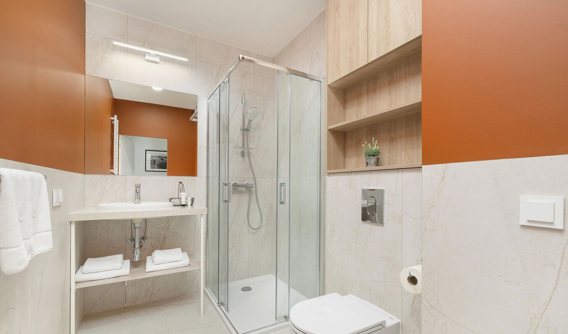 A modern bathroom with a glass-enclosed shower, a white sink, and a toilet.