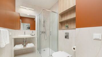 A modern bathroom with a glass-enclosed shower, a white sink, and a toilet.