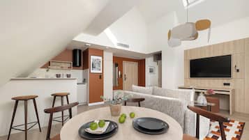 A modern kitchen with a dining area, a TV, and a staircase leading to an upper level.