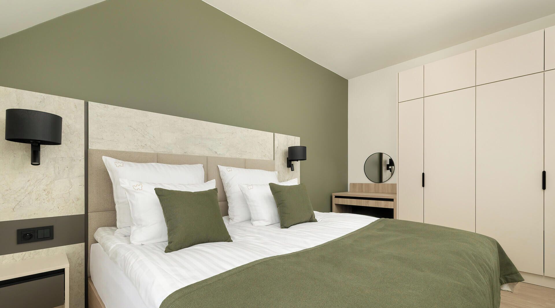 Een keurig opgeruimde hotelkamer met een bed, nachtkastjes, een kledingkast en een spiegel.