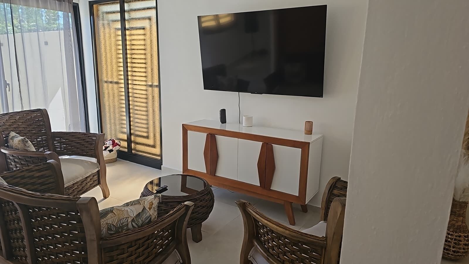 A living room with a flat-screen TV mounted on the wall, wicker furniture, and a white console table.