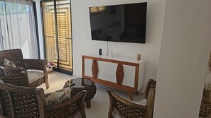 Ein Wohnzimmer mit einem wandmontierten Flachbildfernseher, Korbmöbeln und einem weißen Konsolentisch.