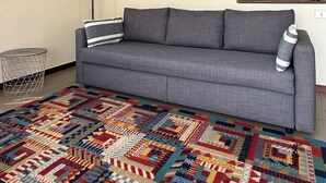 A living room with a grey sofa, a colorful rug, two framed paintings, a lamp, and a small side table.