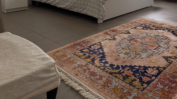 A bedroom with a bed, bedside tables, a nightstand, a window with curtains, and a patterned rug.