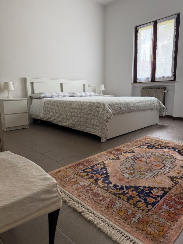 Un dormitorio con una cama, mesitas de noche, cortinas en una ventana y una alfombra estampada.