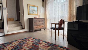 A living room with a patterned rug, a wooden chair, a dark wooden cabinet, a television, and a staircase leading to another room.