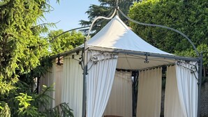 A gazebo with a table and chairs, surrounded by a garden with purple flowers.