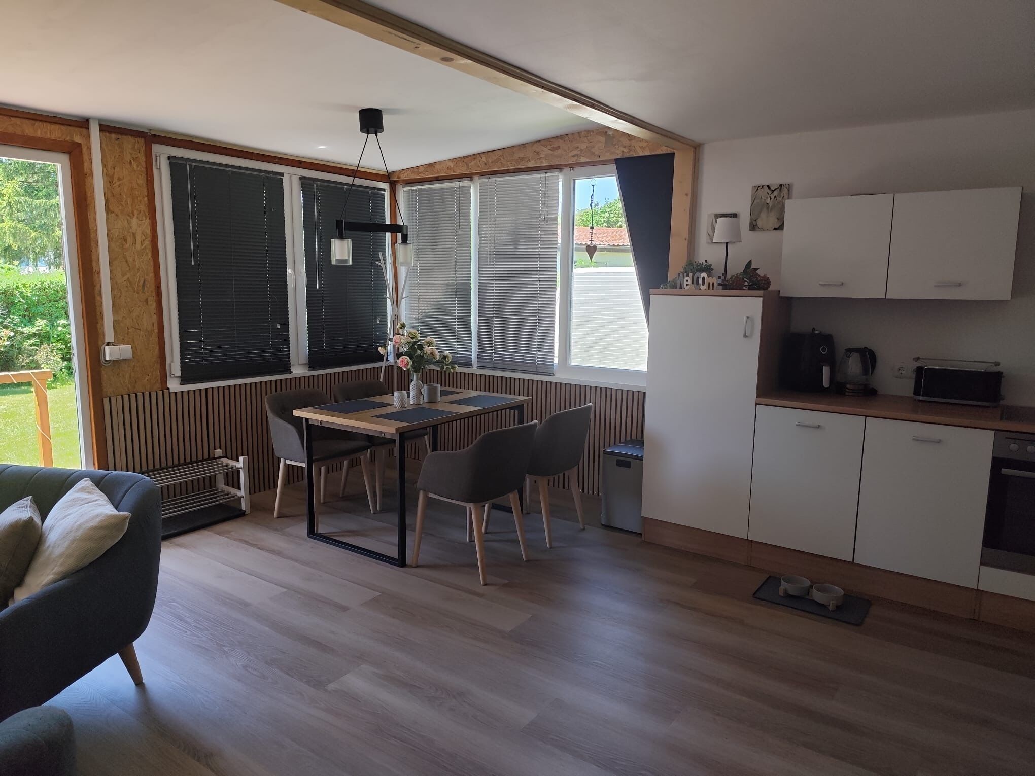Une cuisine moderne avec des meubles blancs, une table à manger avec des chaises et une vue sur l’extérieur grâce à de grandes fenêtres.