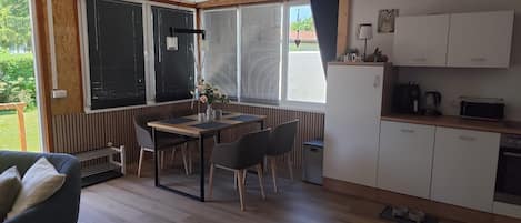 Een moderne keuken met witte kastjes, een eettafel met stoelen en uitzicht op het landschap door grote ramen.