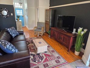 A living room with a dark brown leather sofa, a wooden coffee table, a television on a wooden stand, and a patterned rug.