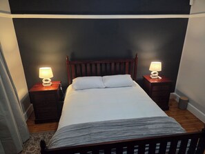 A bed with white bedding, flanked by two bedside tables with lamps, in a room with dark walls and wooden flooring.